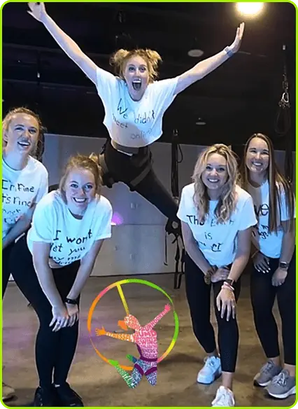 A bachelorette group in matching shirts laughing in the studio while one friend flies mid-air on a bungee cord