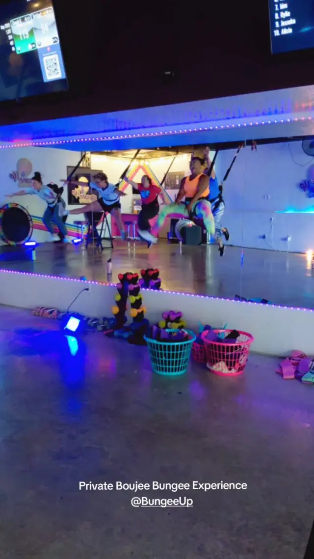A private Boujee Bungee Experience under blue studio lighting, guests suspended at their stations with kit baskets lined up along the mirror